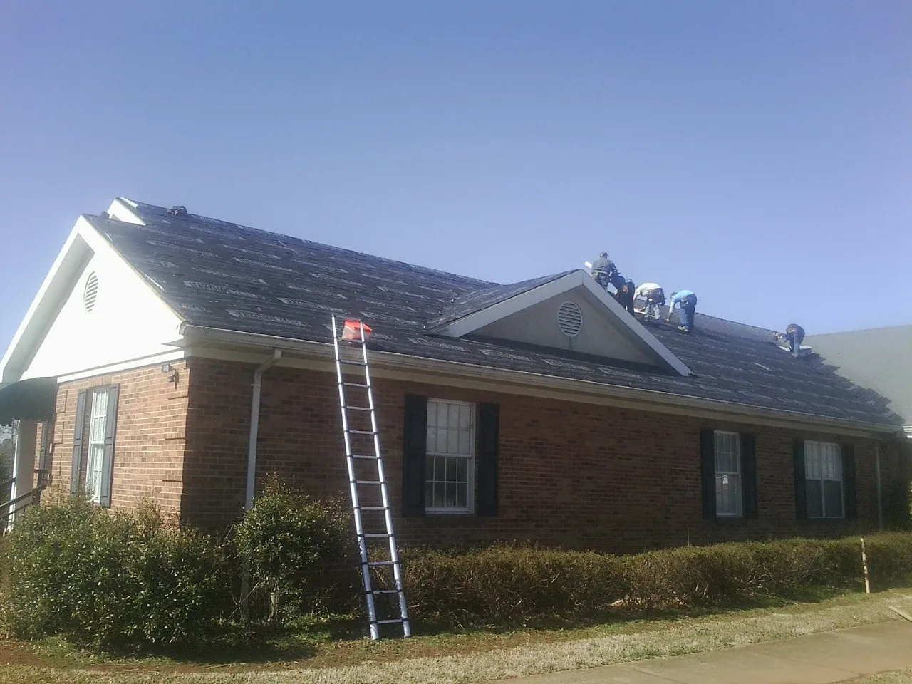 Crew tearing shingles off a brick ranch roof with a ladder set — Metal Roof Repair work by our crew in South Haven