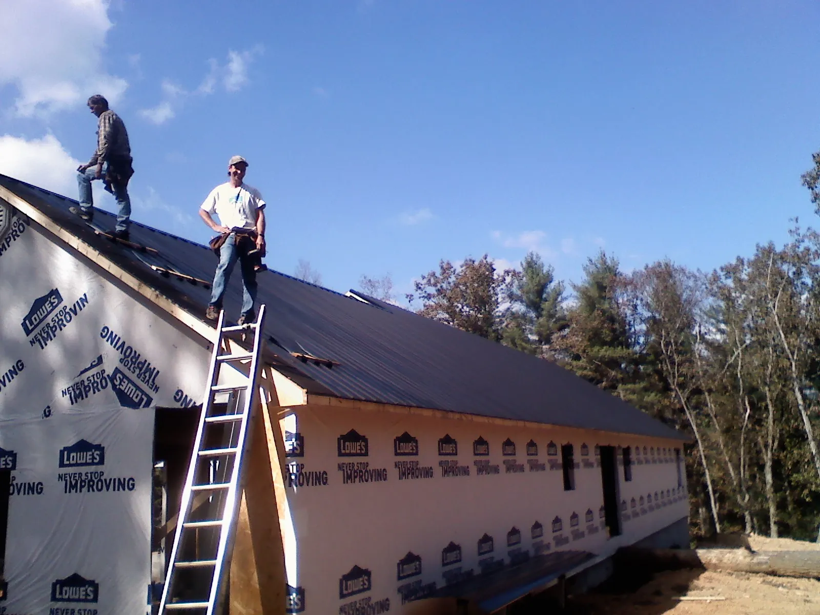 Two roofers standing on a long dark metal roof over a wrapped building in South Haven