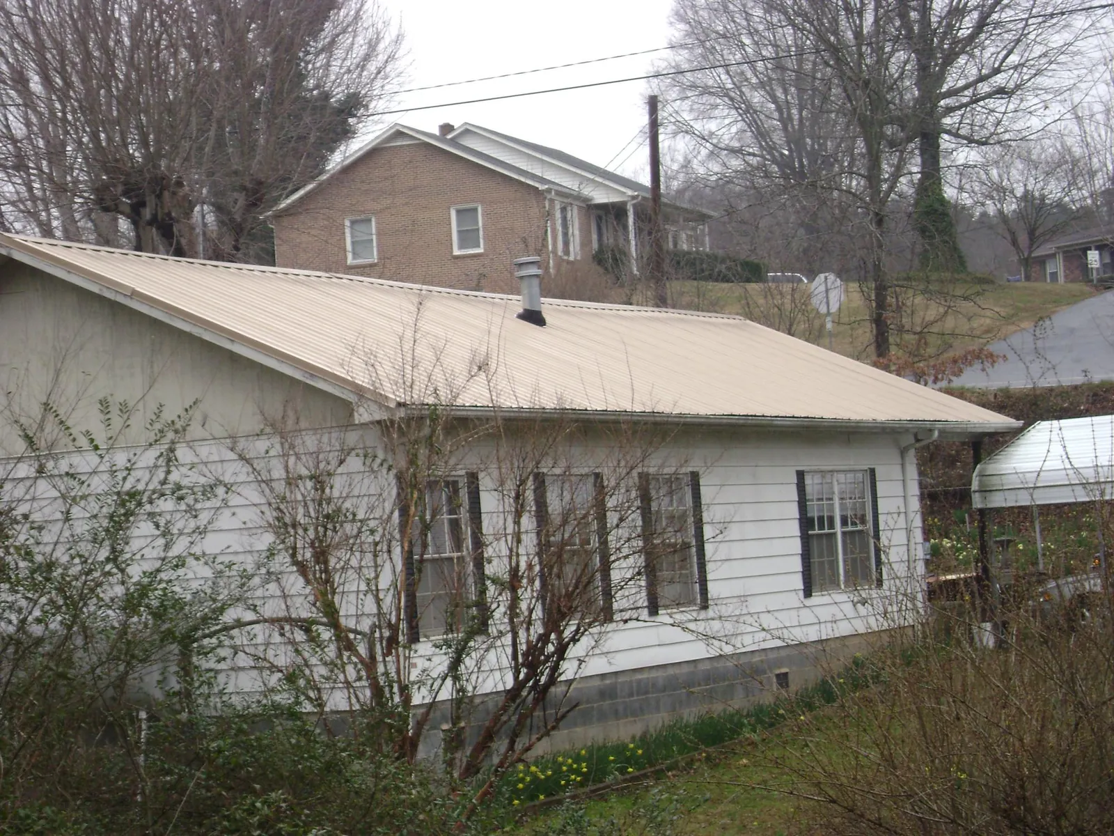 Tan metal roof on a white sided house set into a hillside — Commercial Roofing by Roofing Brothers in South Haven